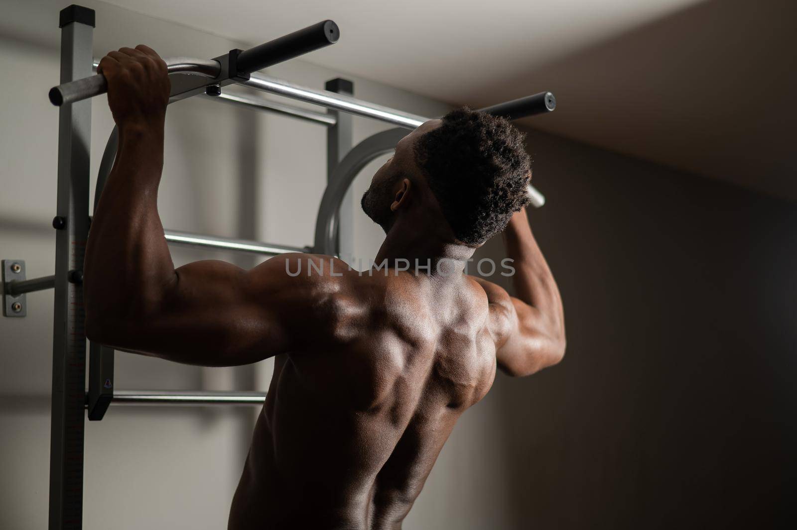 African american man with naked torso pulls up on horizontal bar in gym. by mrwed54