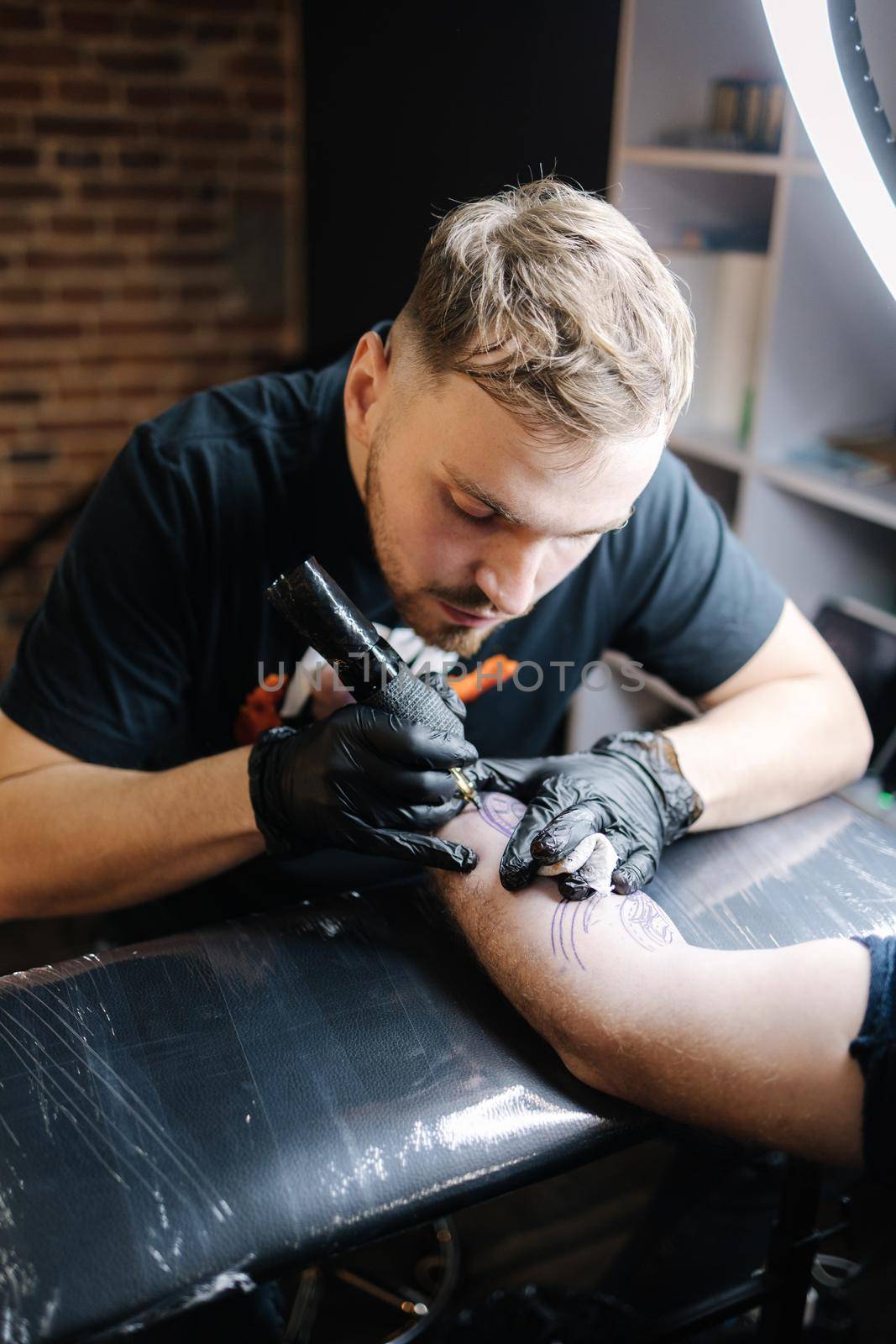 Tattoo master is tattooing a man's hand. Tattoo machine, safety and hygiene at work. Close-up of tattoo artist work. Tattoo salon.