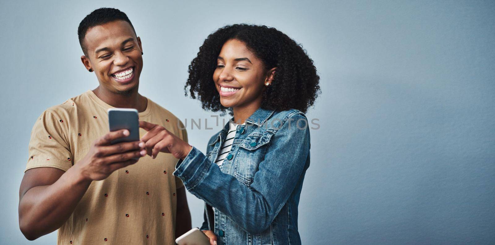 Studio shot of a young man and woman using a mobile phone together against a gray background.