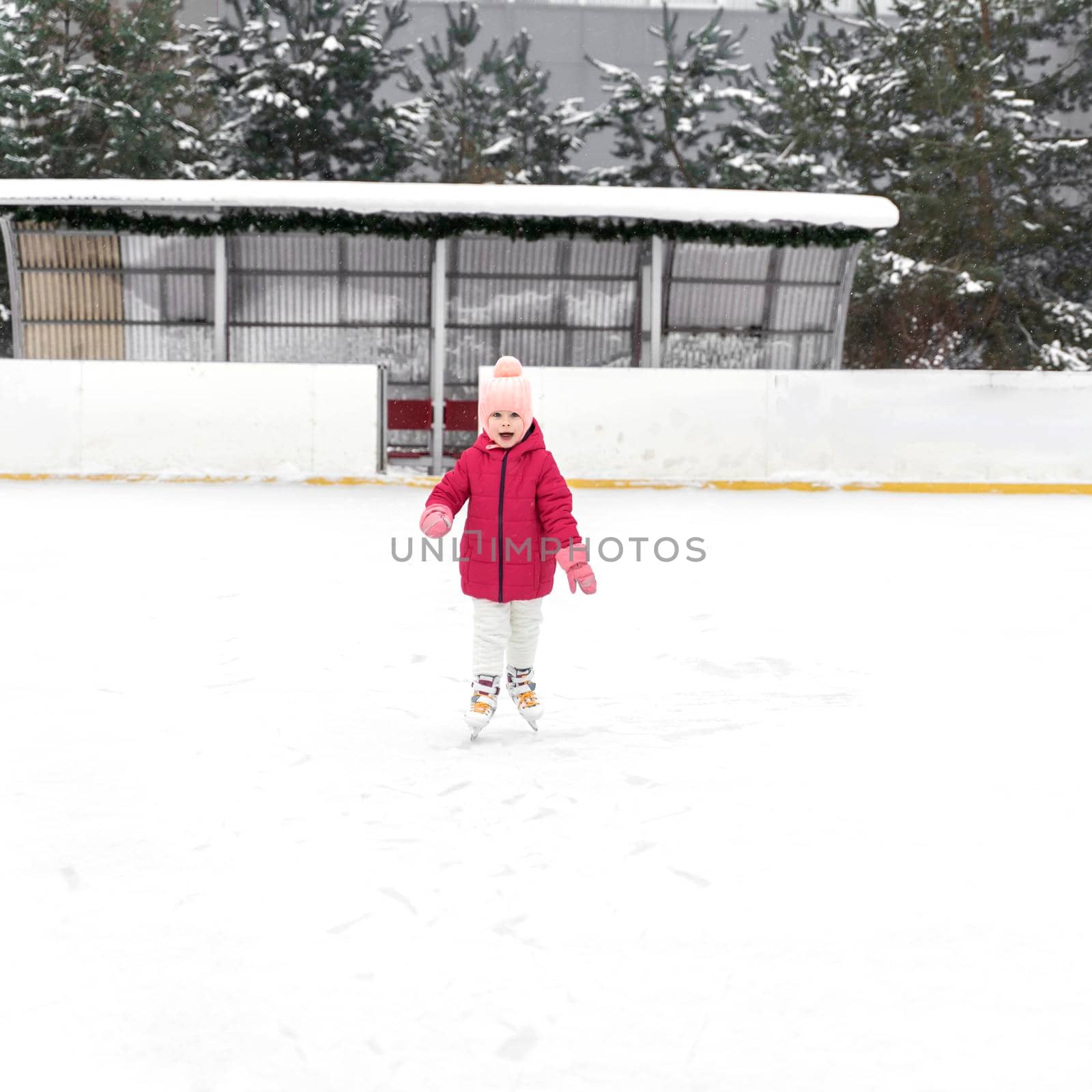 kid girl in a red jacket skates on a skating rink outdoors