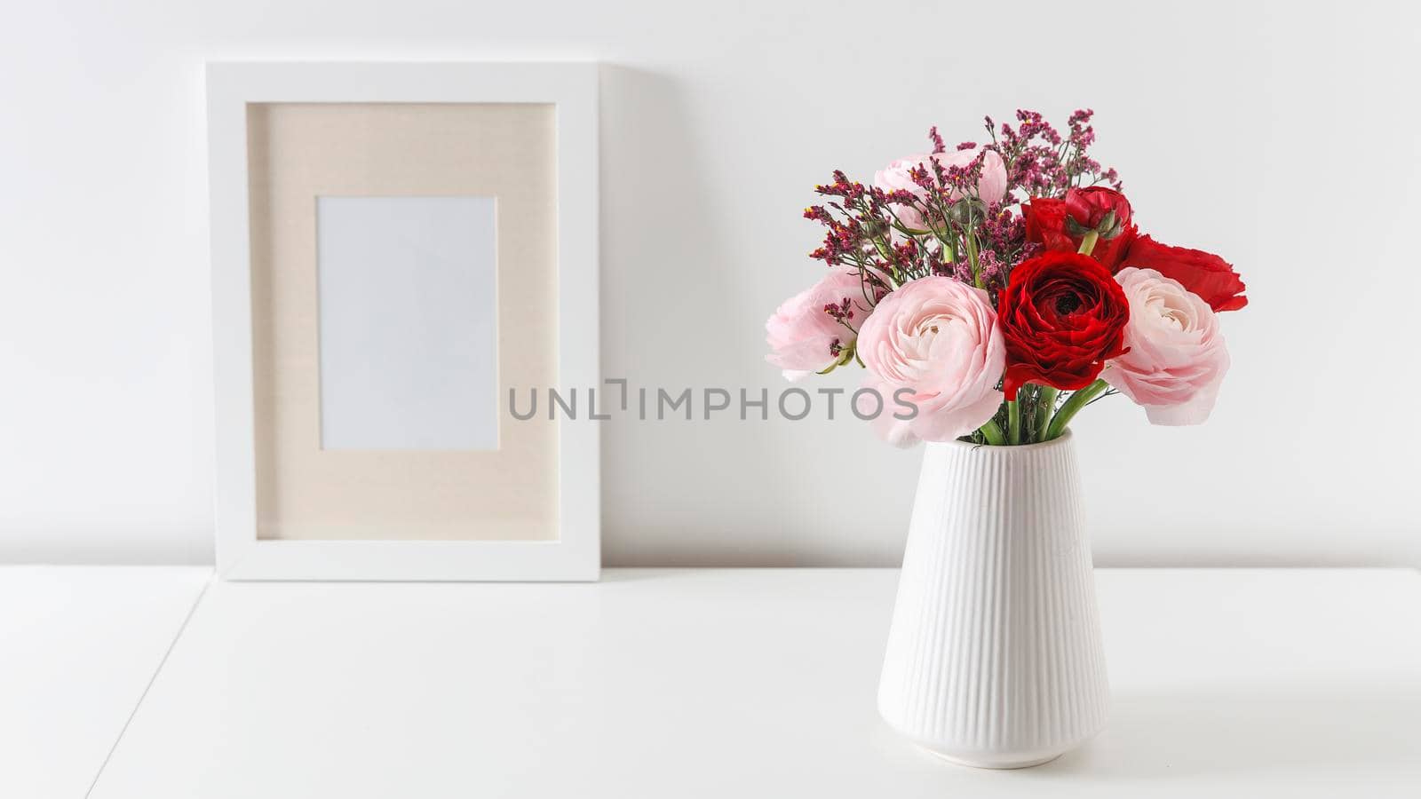 Bouquet of red and pink Persian buttercups on a white table. Scandinavian style. Place for text. Copy space by elenarostunova