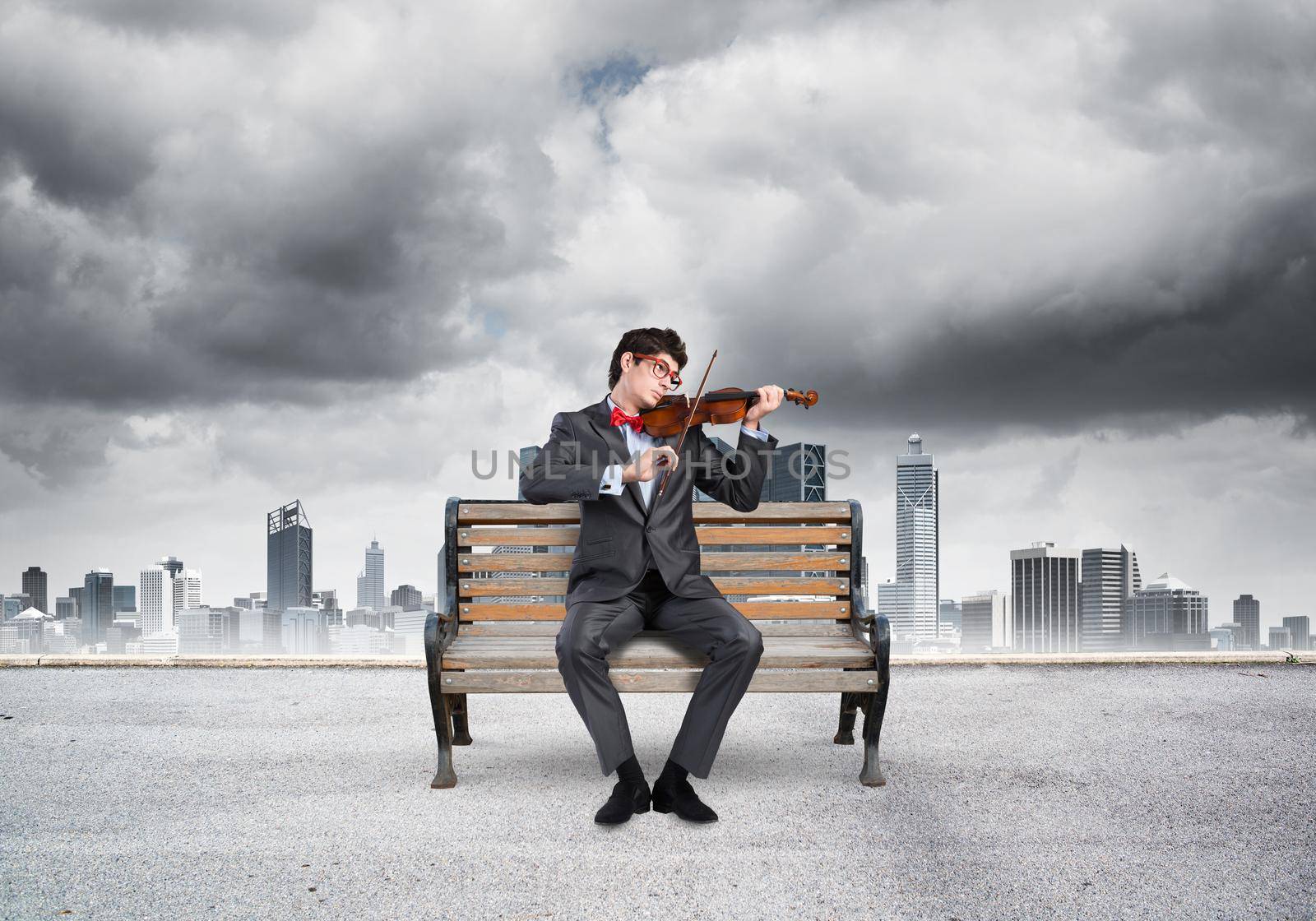 Young businessman plays the violin sitting on a wooden bench. Inspiration in business