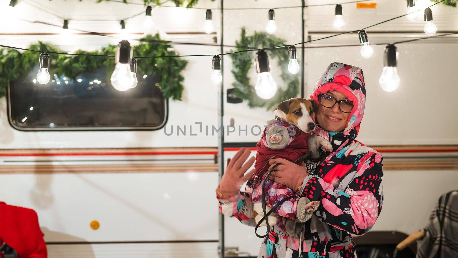 Caucasian woman holding Jack Russell Terrier dog by the trailer. Christmas van decorated by mrwed54