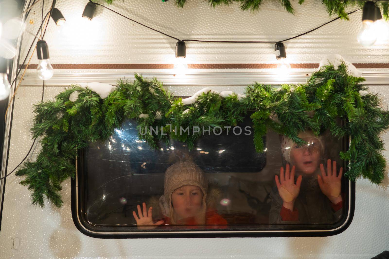 Two boys look out of the window of a Christmas-decorated camper
