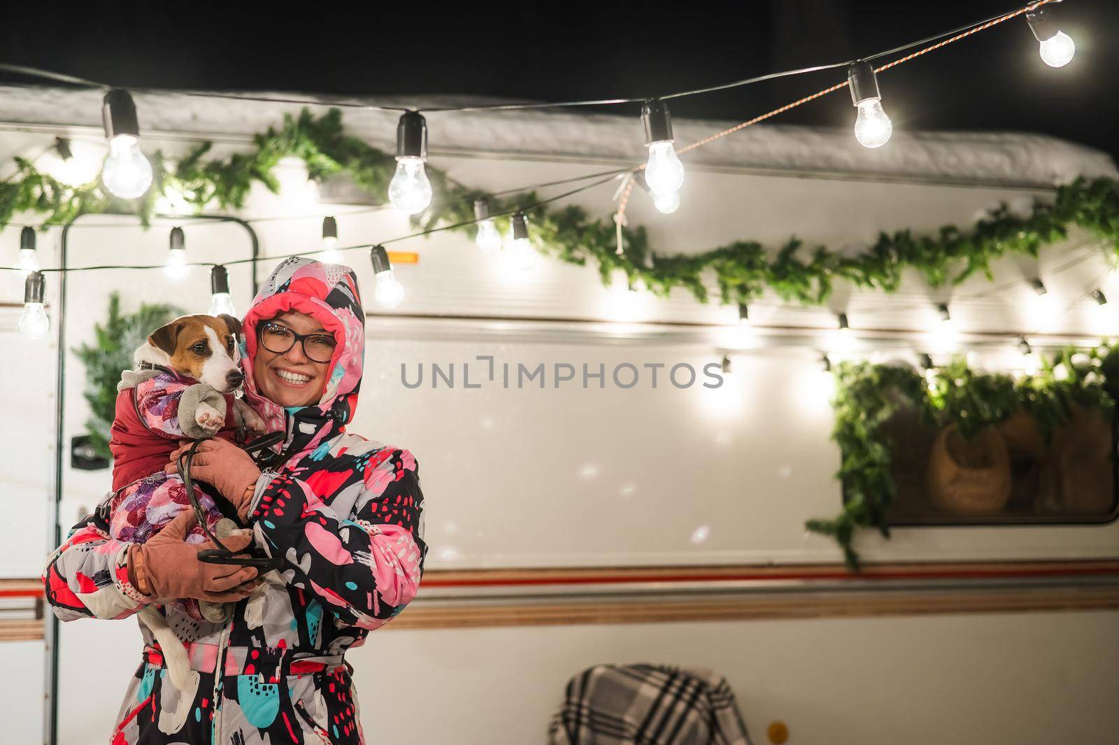Caucasian woman holding Jack Russell Terrier dog by the trailer. Christmas van decorated by mrwed54