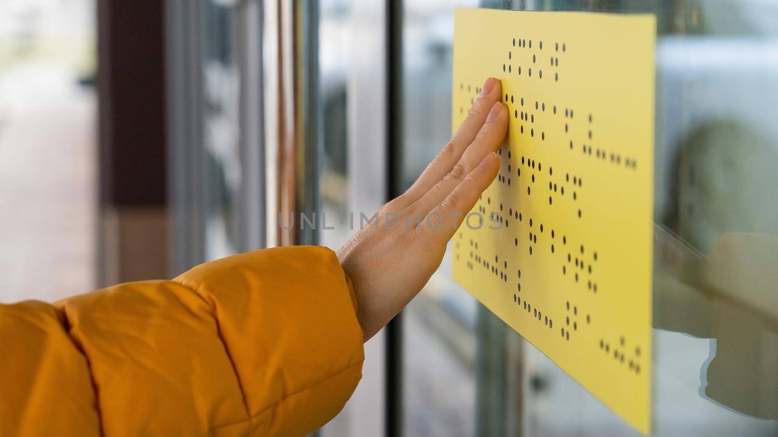Close-up of a woman reading a braille lettering on a glass door. by mrwed54