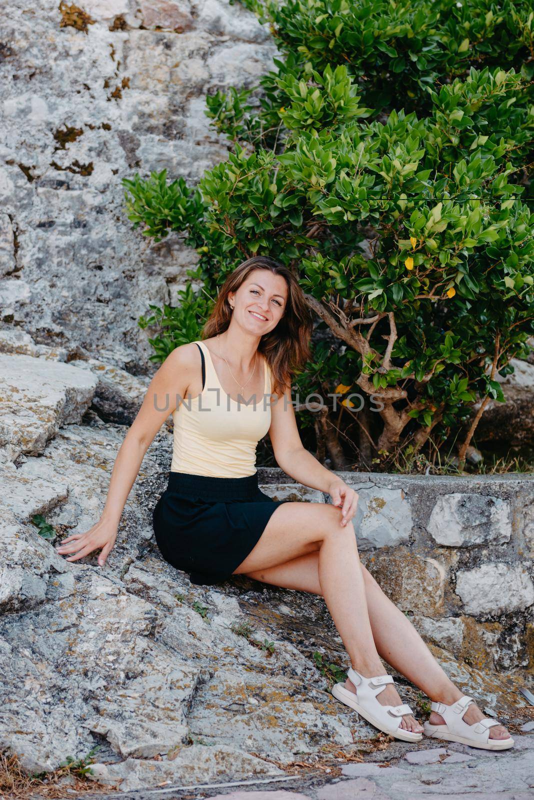 Beautiful girl sits on the stone wall of the old town of Budva . The girl sits on a stone parapet, Budva, Montenegro