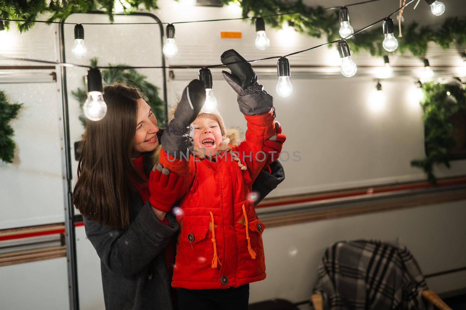 Caucasian woman and son decorate camper for christmas. Happy family travels in a mobile home