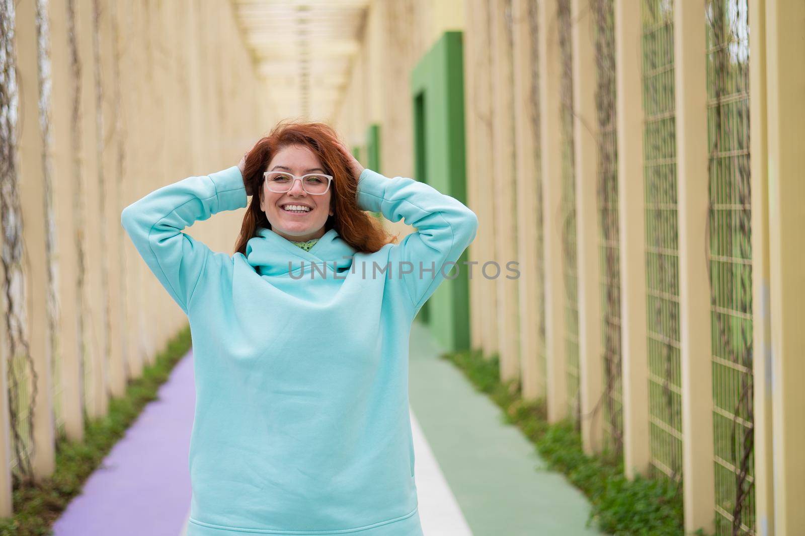 Caucasian red-haired woman in a mint hoodie walking in the park. by mrwed54
