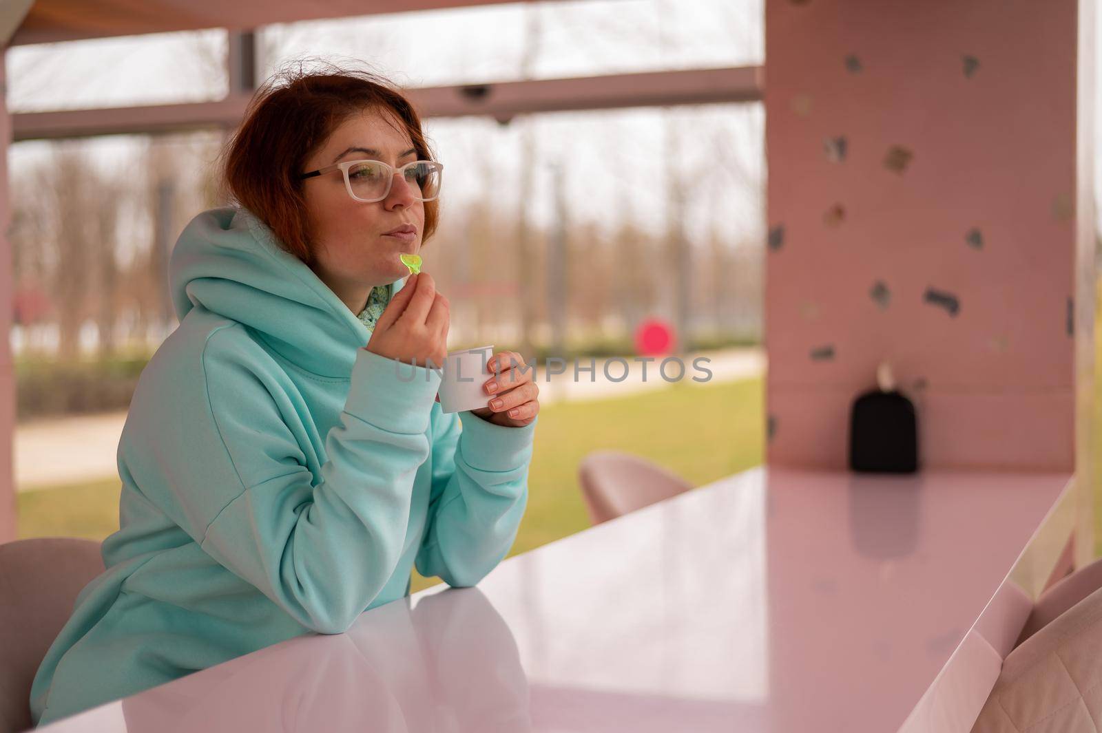 Caucasian red-haired woman eats ice cream with a plastic spoon while sitting alone in a cafe. by mrwed54