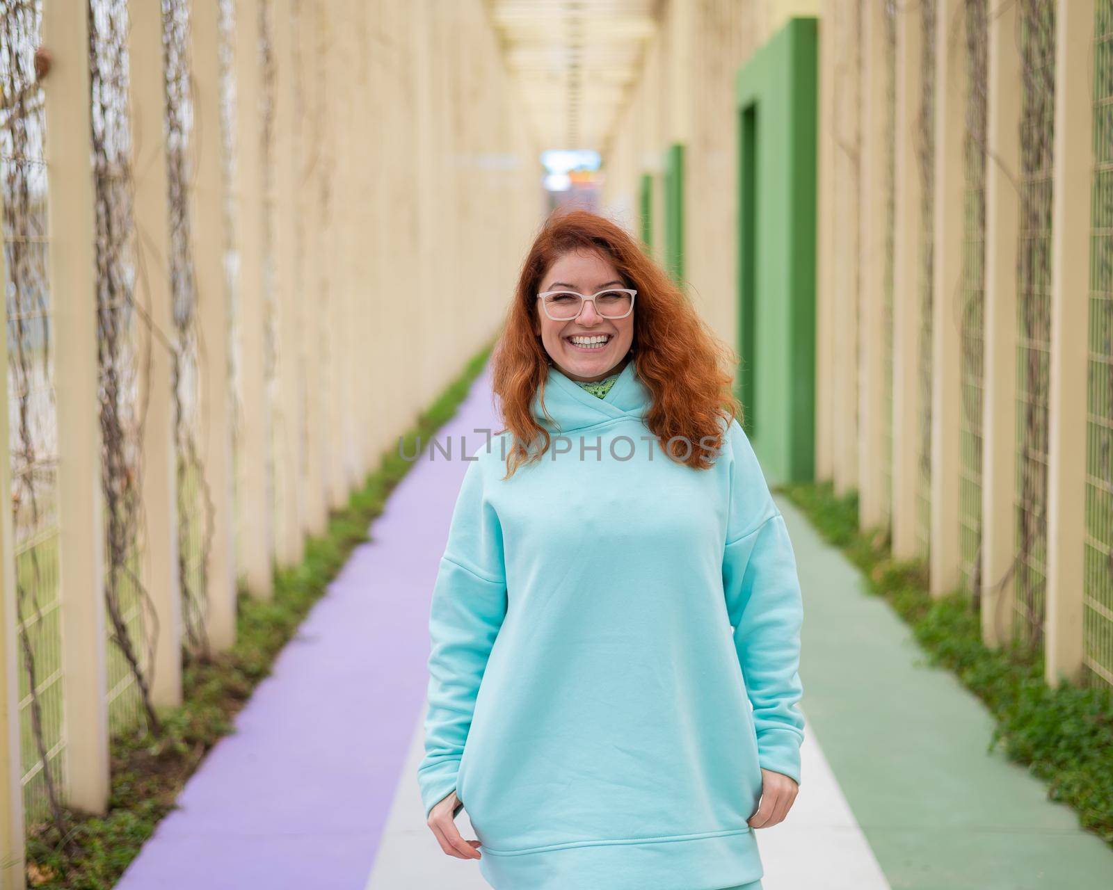 Caucasian red-haired woman in a mint hoodie walking in the park