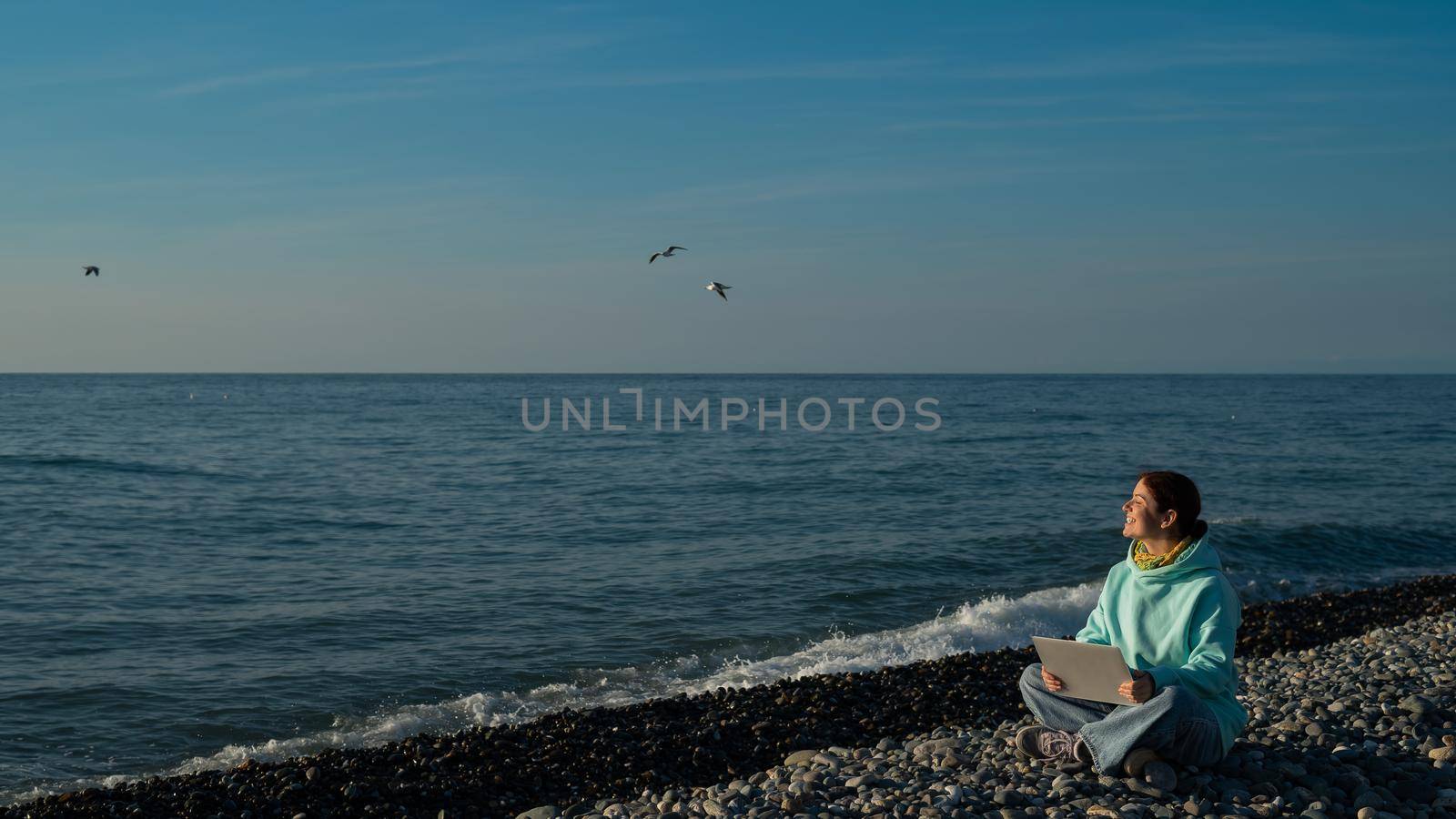 Happy caucasian woman working on a laptop while sitting on a pebble beach. by mrwed54