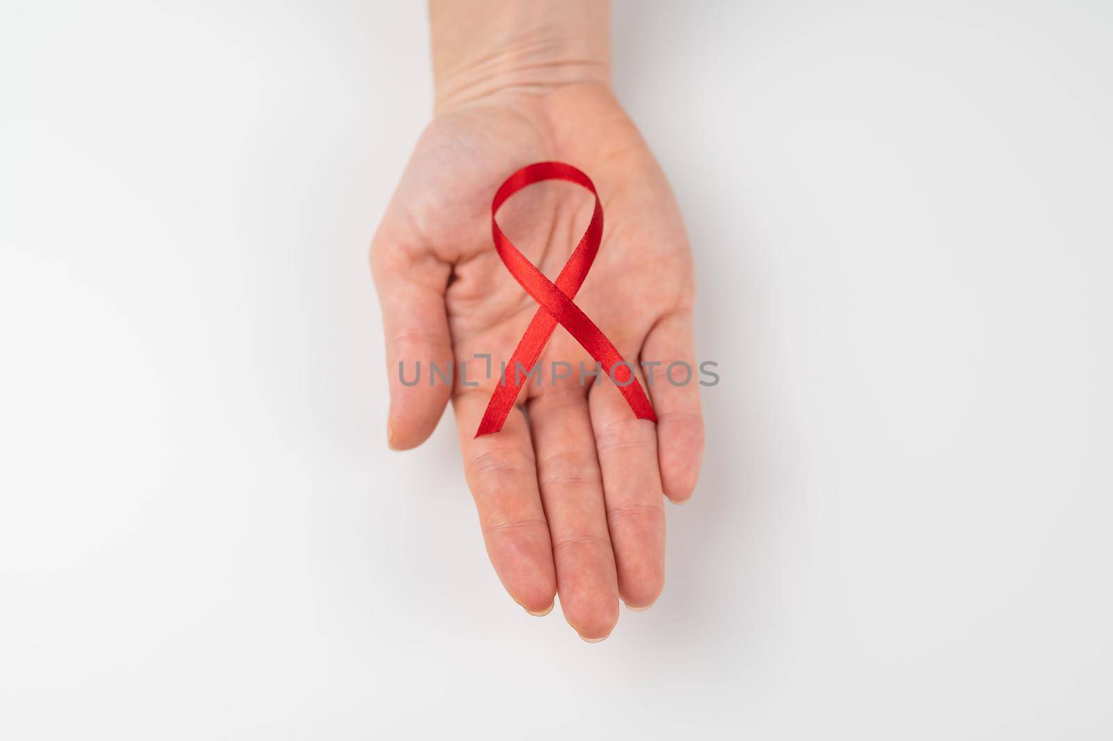 Female palm with a red ribbon on a white background. Symbol of the fight against AIDS