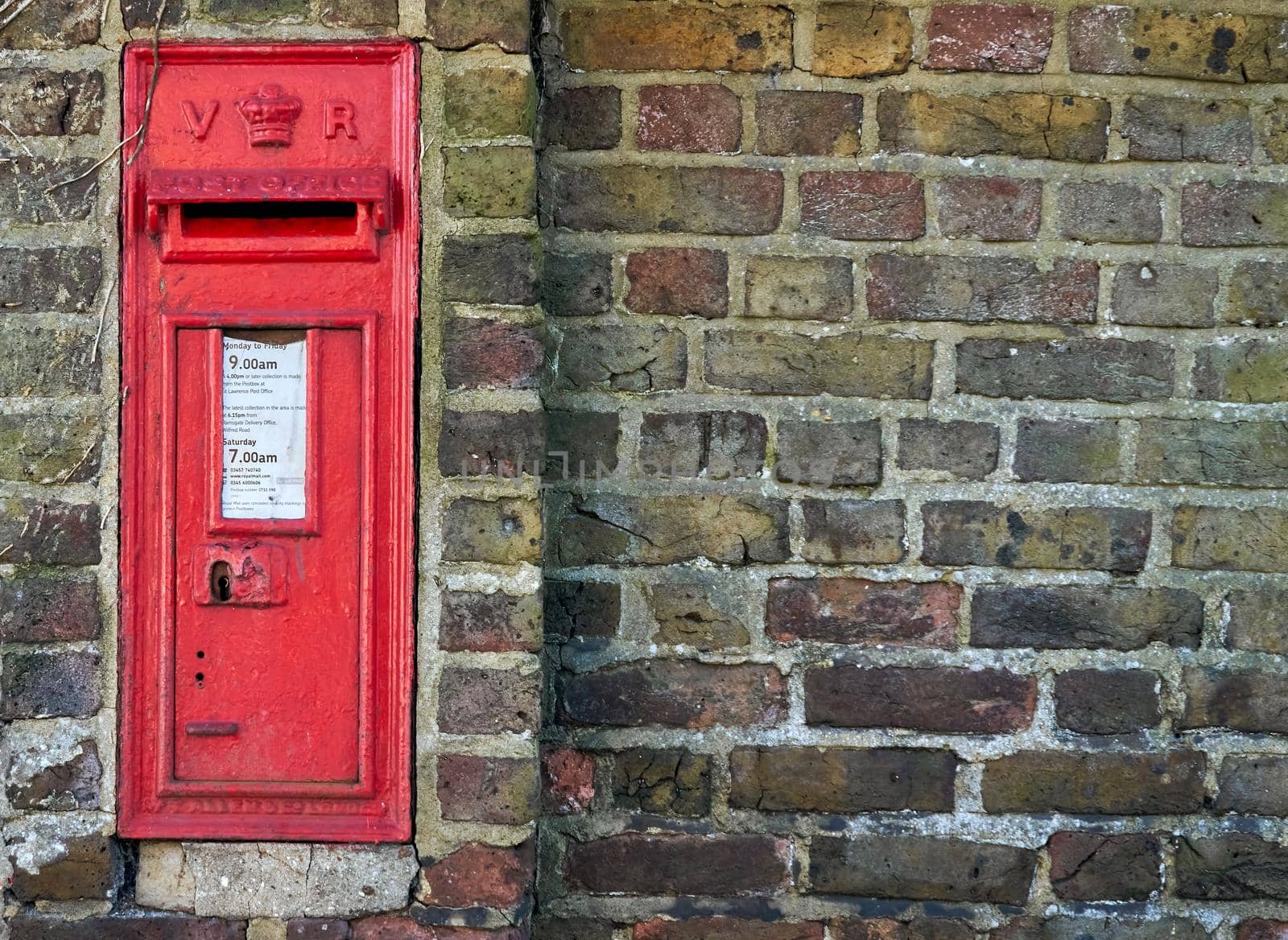 A red British post box in a wall with the royal cypher VR by ChrisWestPhoto