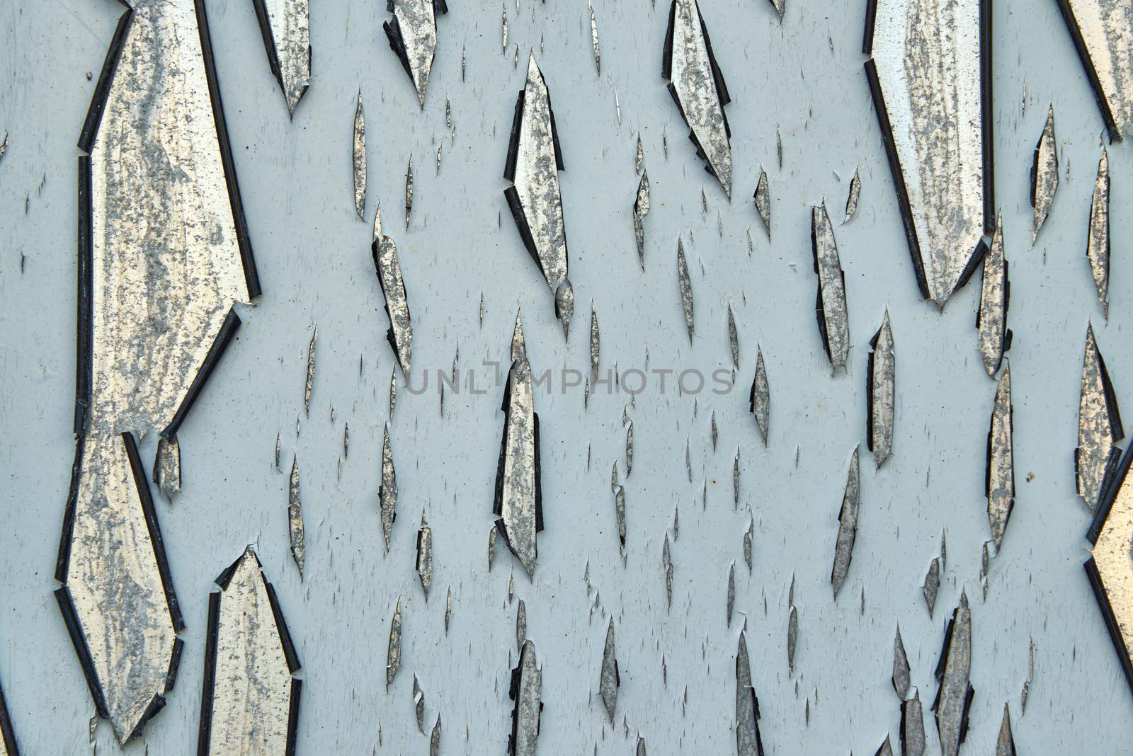 Grey paint cracks and peels off of a reflective metallic surface