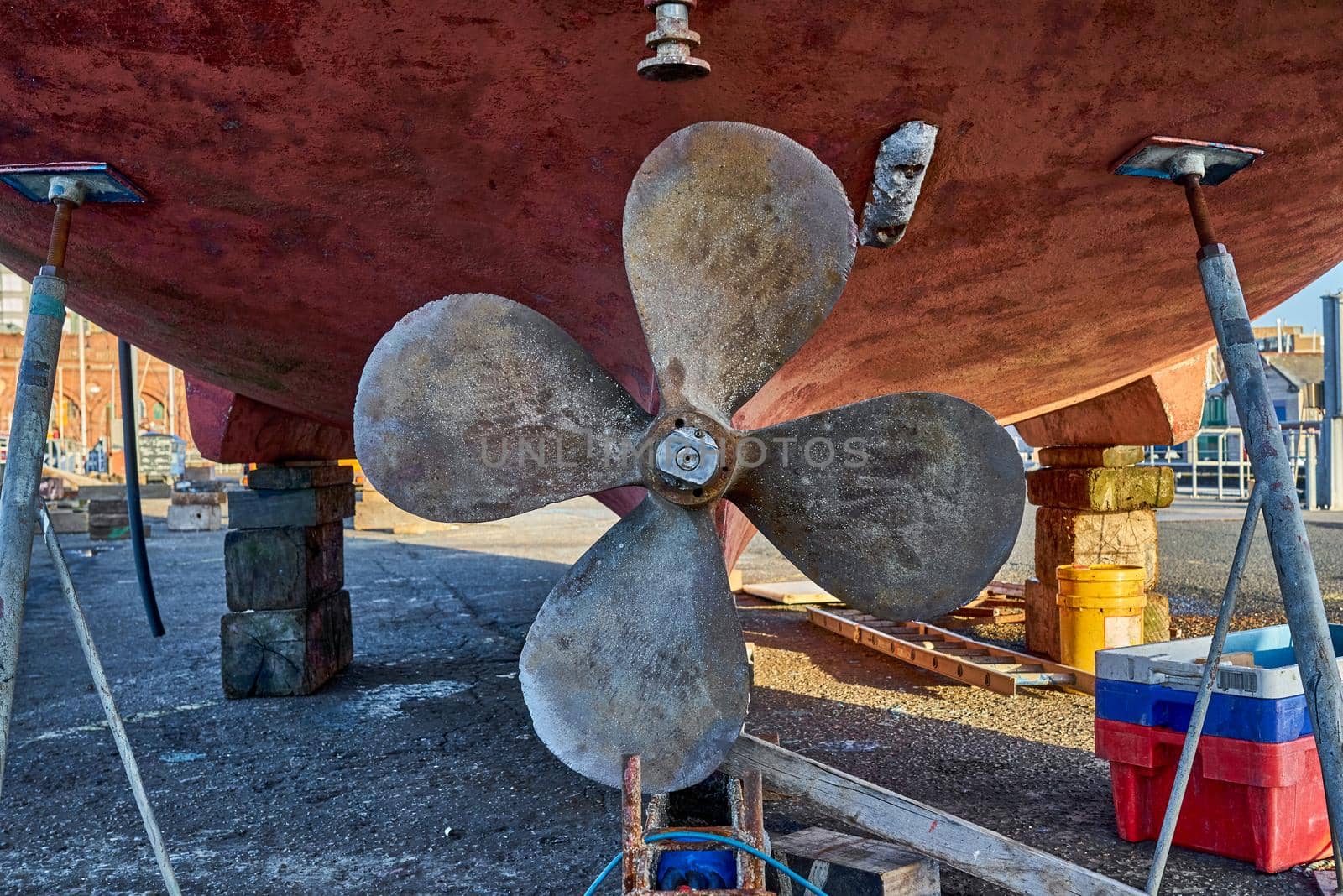 A red ship in dry dock showing the propeller from the back