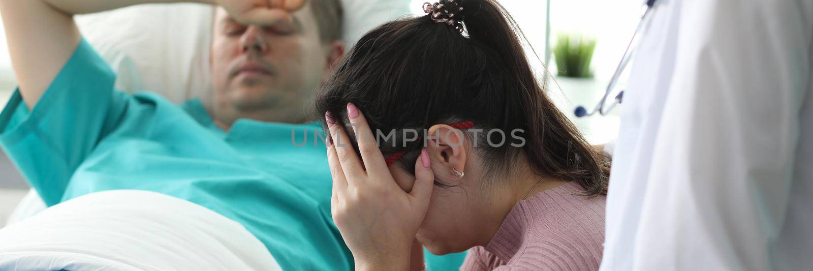 Girl crying near man lying on bed in ward clinic. Monitoring all vital functions patient. Medicine use modern and proven practice diagnostic and treatment methods. Preoperative preparation