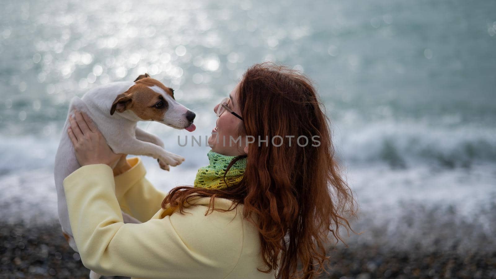 Caucasian red-haired woman holding a dog jack russell terrier on the seashore