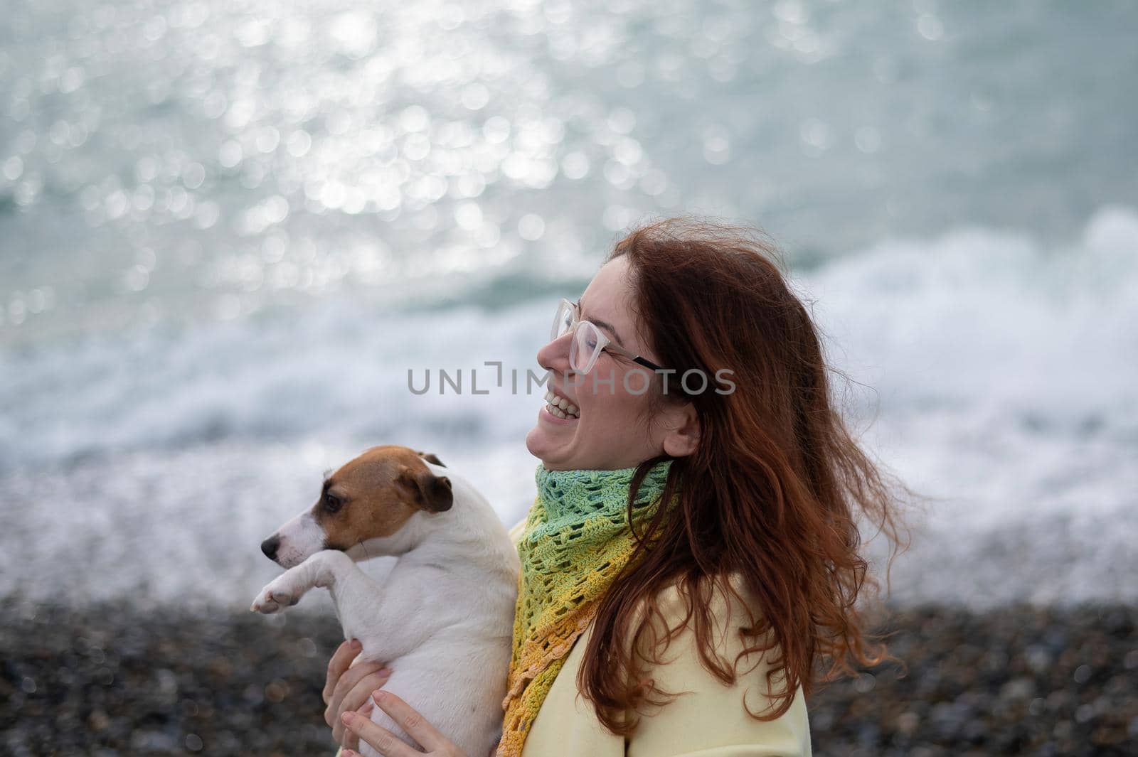 Caucasian red-haired woman holding a dog jack russell terrier on the seashore