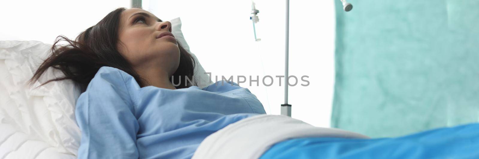 Closeup of young woman laying in hospital bed and waiting for analysis. Clinic patient. Treatment with drop bottle. Medicine and health diagnostic concept