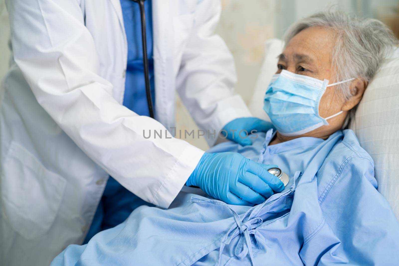 Doctor using stethoscope to checking Asian senior or elderly old lady woman patient wearing a face mask in hospital for protect infection Covid-19 Coronavirus. by pamai