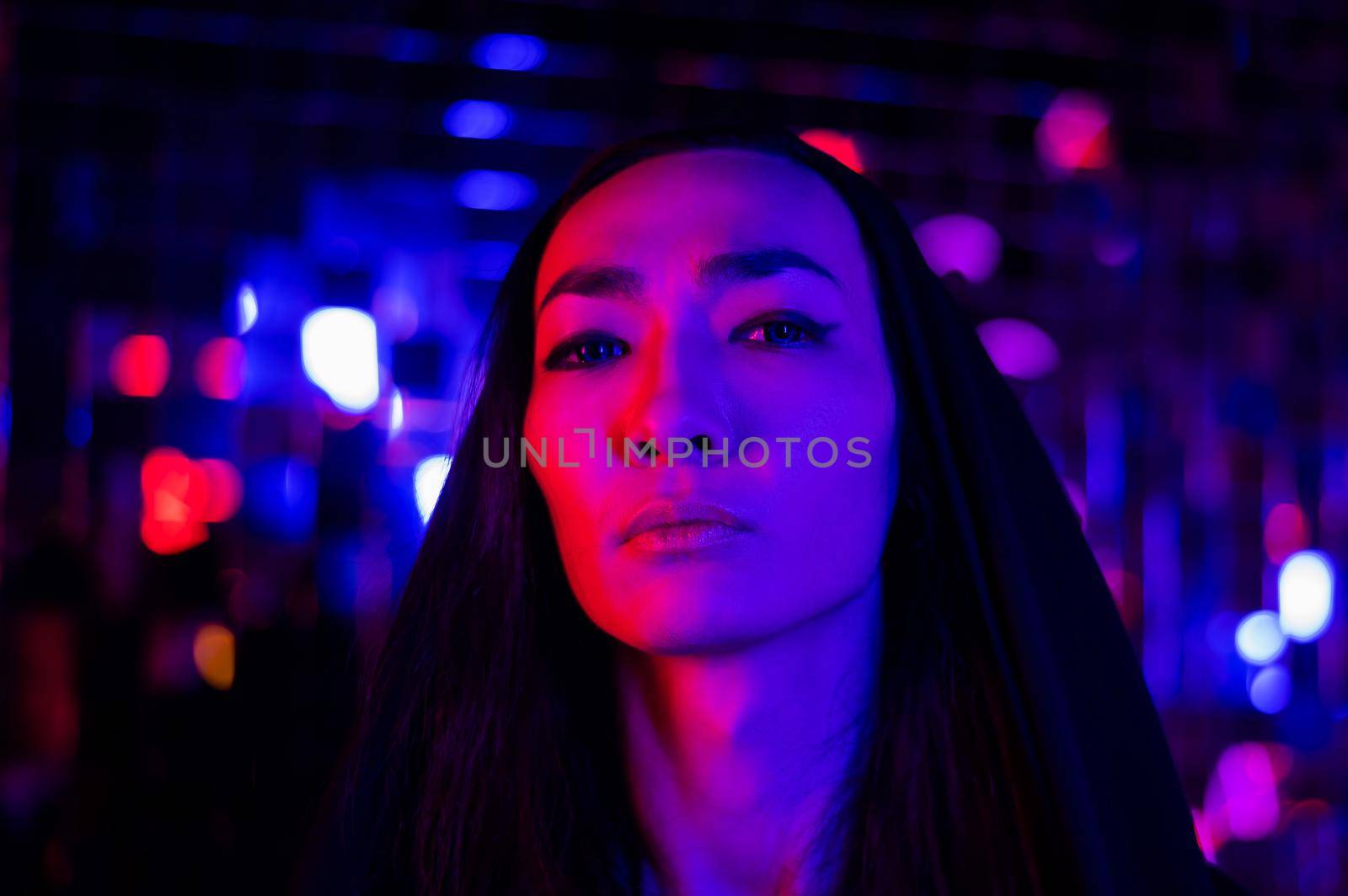 Close-up portrait of an androgenic model in a hood. Male transgender in studio with neon light