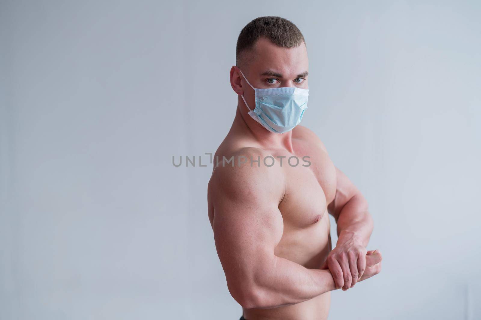 Bodybuilder with a naked torso in a medical mask. Muscled with a guy doing sports in quarantine. Respiratory protection