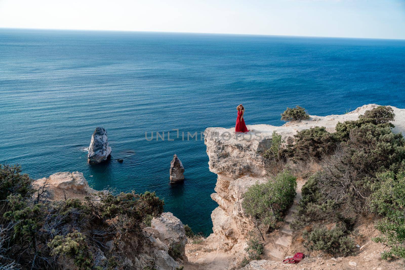 A woman in a red flying dress fluttering in the wind, against the backdrop of the sea. by Matiunina