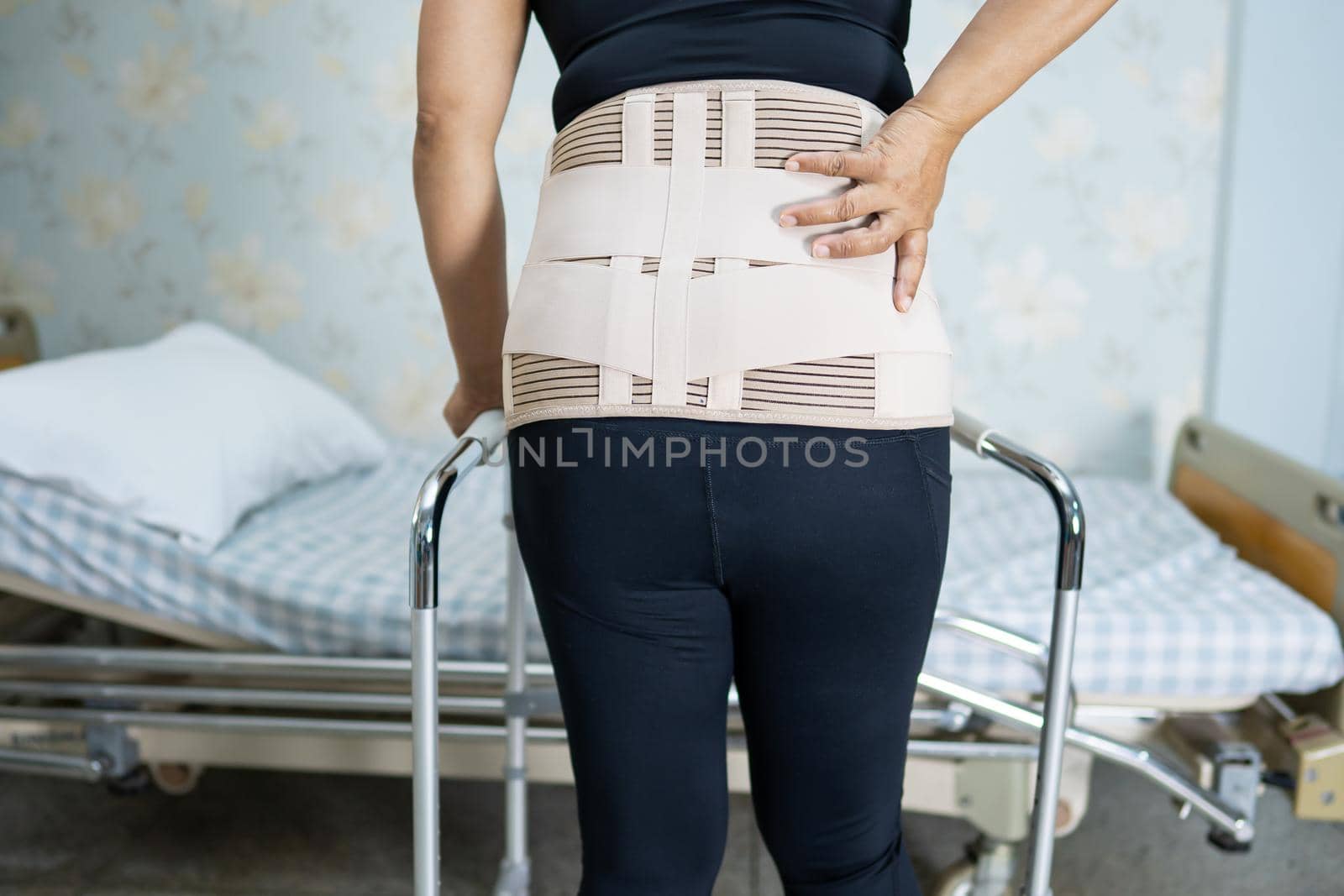 Asian lady patient wearing back pain support belt for orthopedic lumbar with walker. by pamai