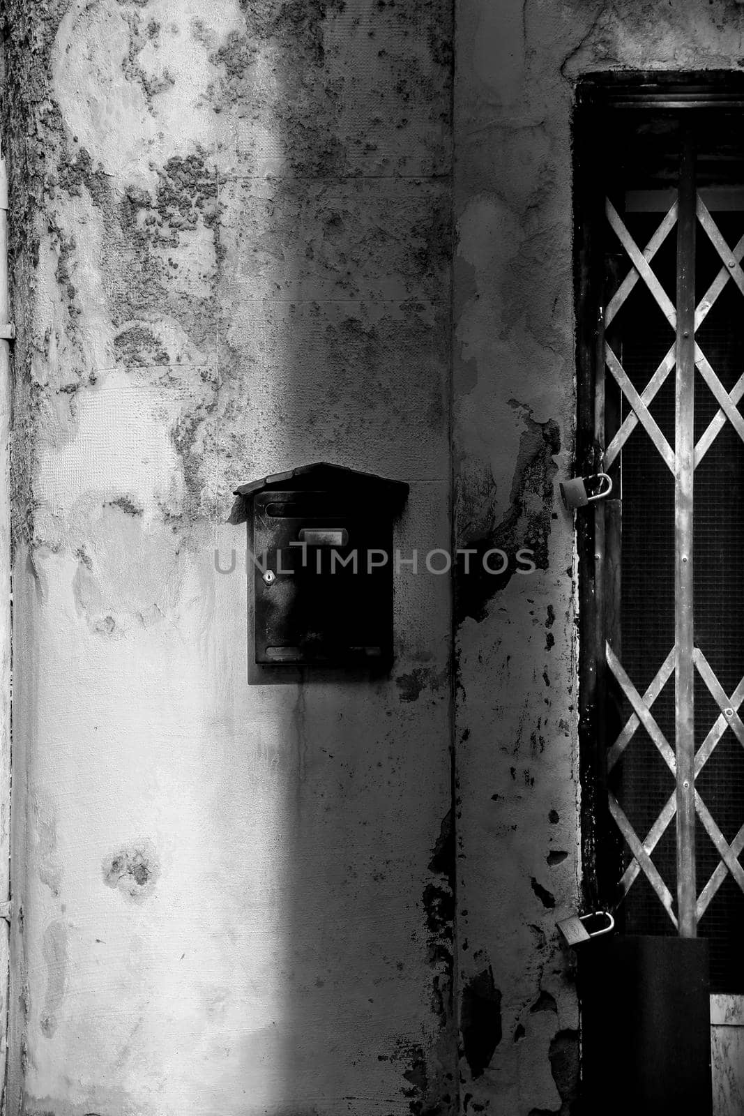 Black mailbox on chipped facade next to door by soniabonet