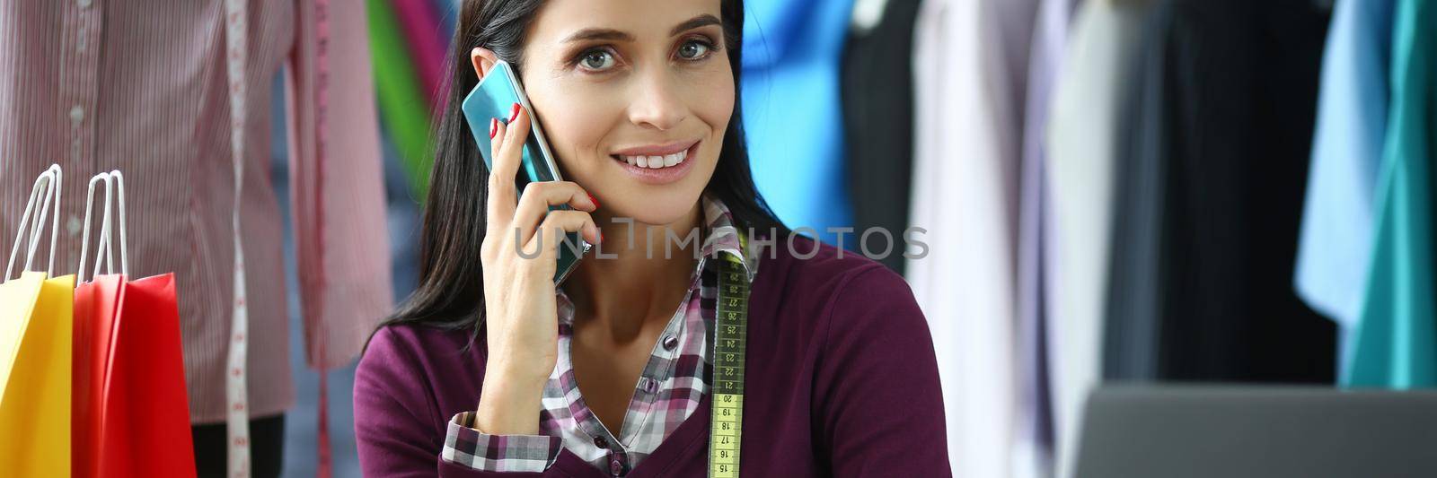 Young woman fashion designer talking on the phone at workplace in atelier. Acceptance of orders for tailoring concept