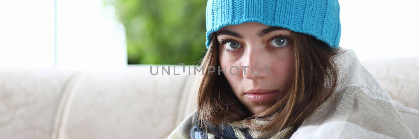 Wrapped young woman is sitting in hat and in plaid with pill. Influenza and seasonal illness concept