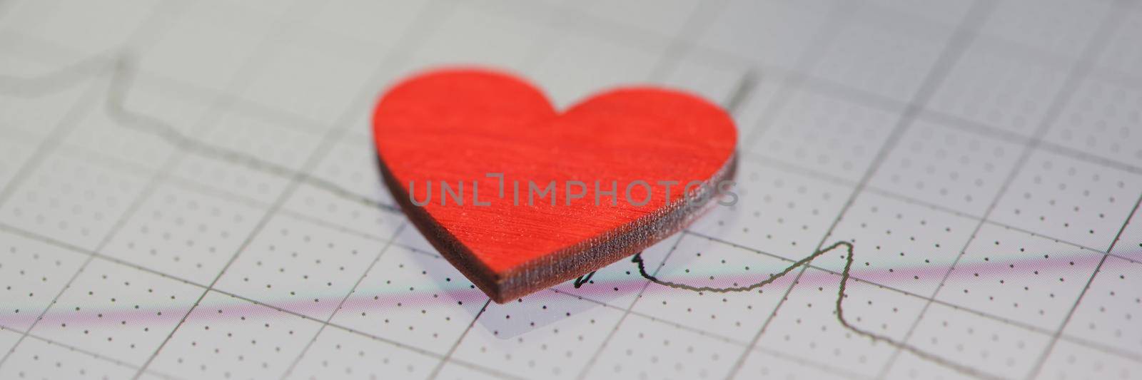 Toy red heart lying on paper with electrocardiogram closeup by kuprevich