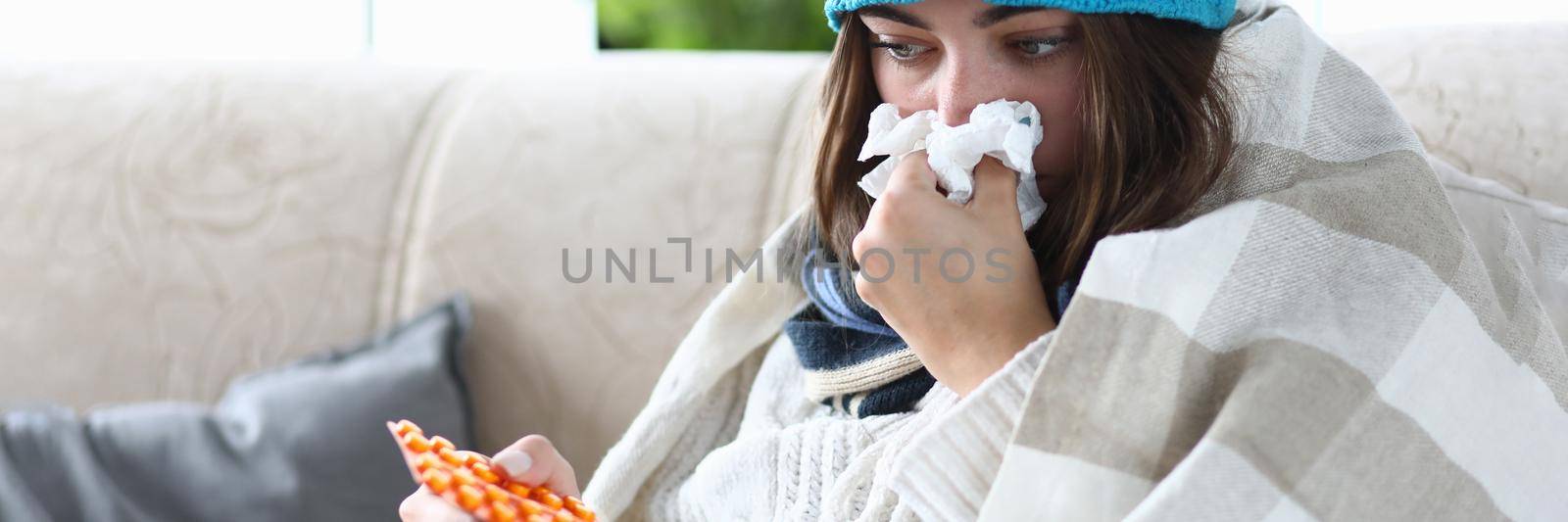 Woman with cold sits on couch with pills and handkerchief. Seasonal disease concept