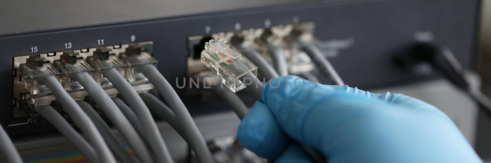 Person working in network server room with fiber optic hub for digital communications and internet. LAN cable is connected to the switch concept