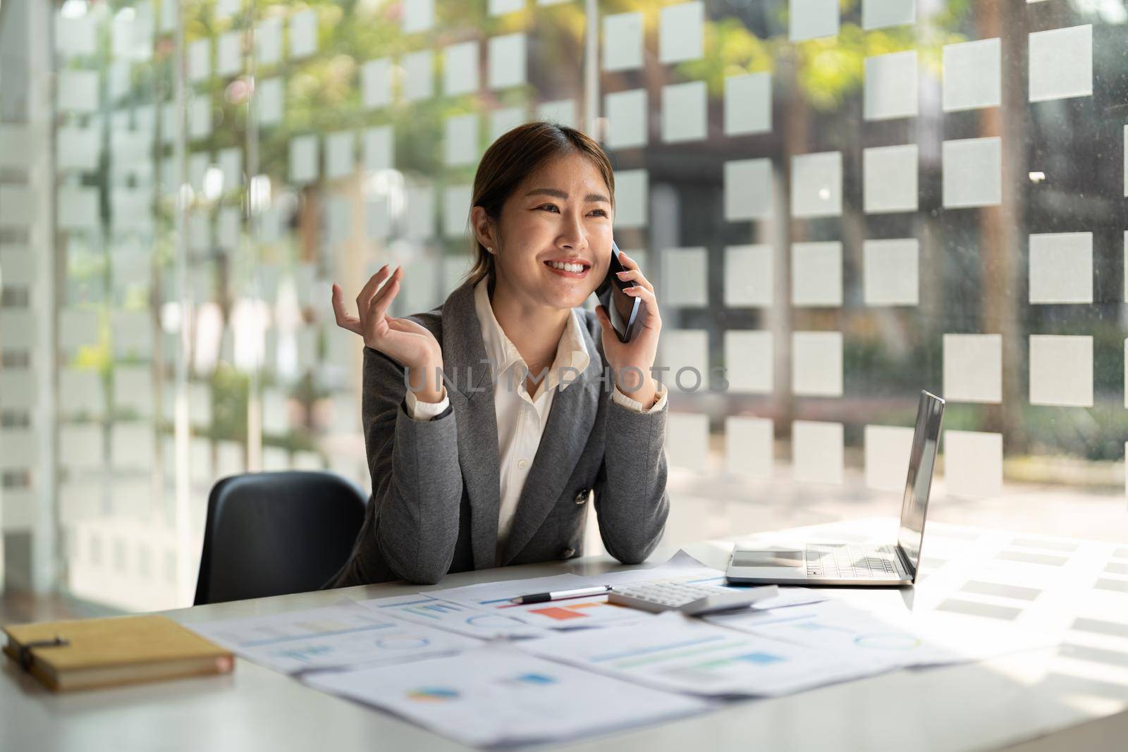 Smiling business asian woman in talking consultant on mobile phone at modern office by nateemee