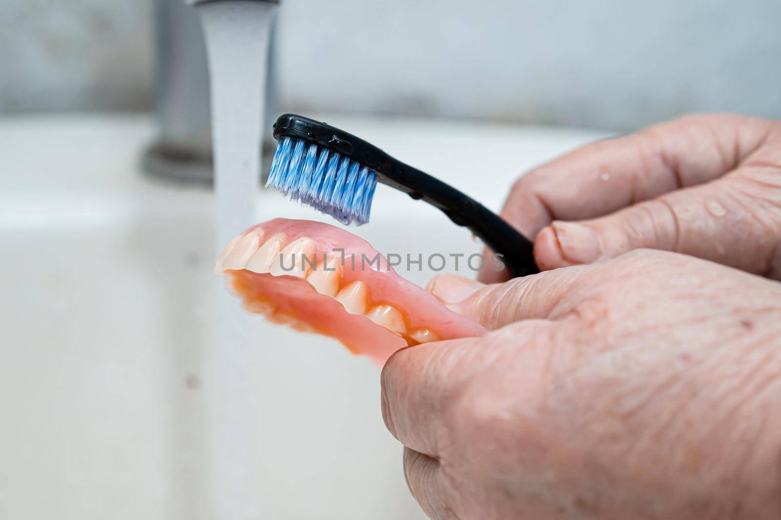 Asian senior or elderly old woman patient use toothbrush to clean partial denture of replacement teeth. by pamai