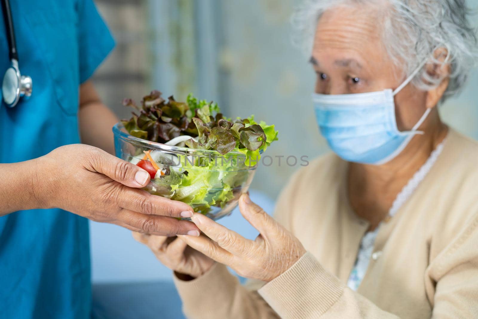 Asian senior or elderly old lady woman patient with mask holding vegetable healthy food with hope and happy while sitting and hungry on bed in hospital.