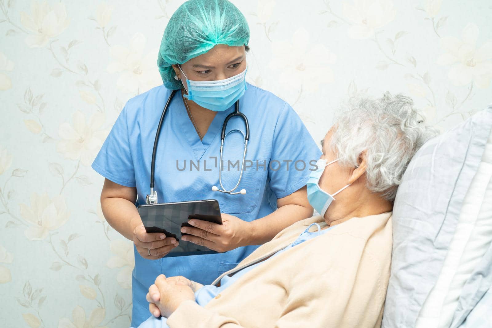 Asian doctor wearing face shield and PPE suit new normal holding tablet to check patient protect safety infection Covid-19 Coronavirus outbreak at quarantine nursing hospital ward.