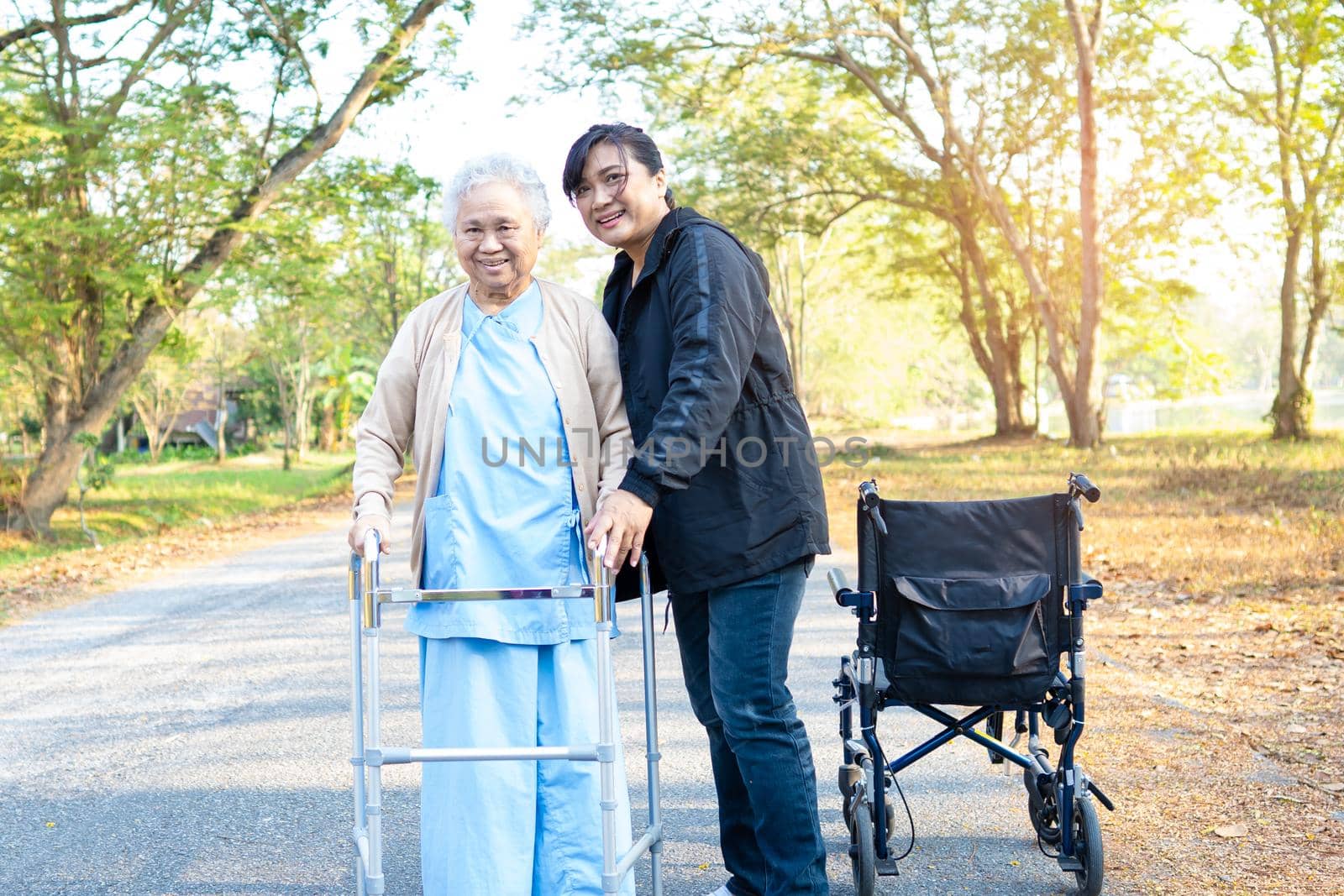 Help and care Asian senior or elderly old lady woman use walker with strong health while walking at park in happy fresh holiday. by pamai