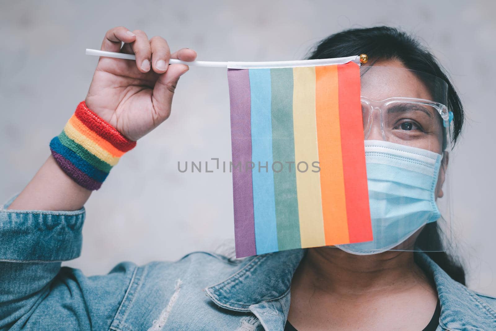 Asian lady wearing mask and face shield for protect covid-19 virus holding rainbow flag, symbol of LGBT pride month celebrate annual in June social of gay, lesbian, bisexual, transgender, human rights. by pamai