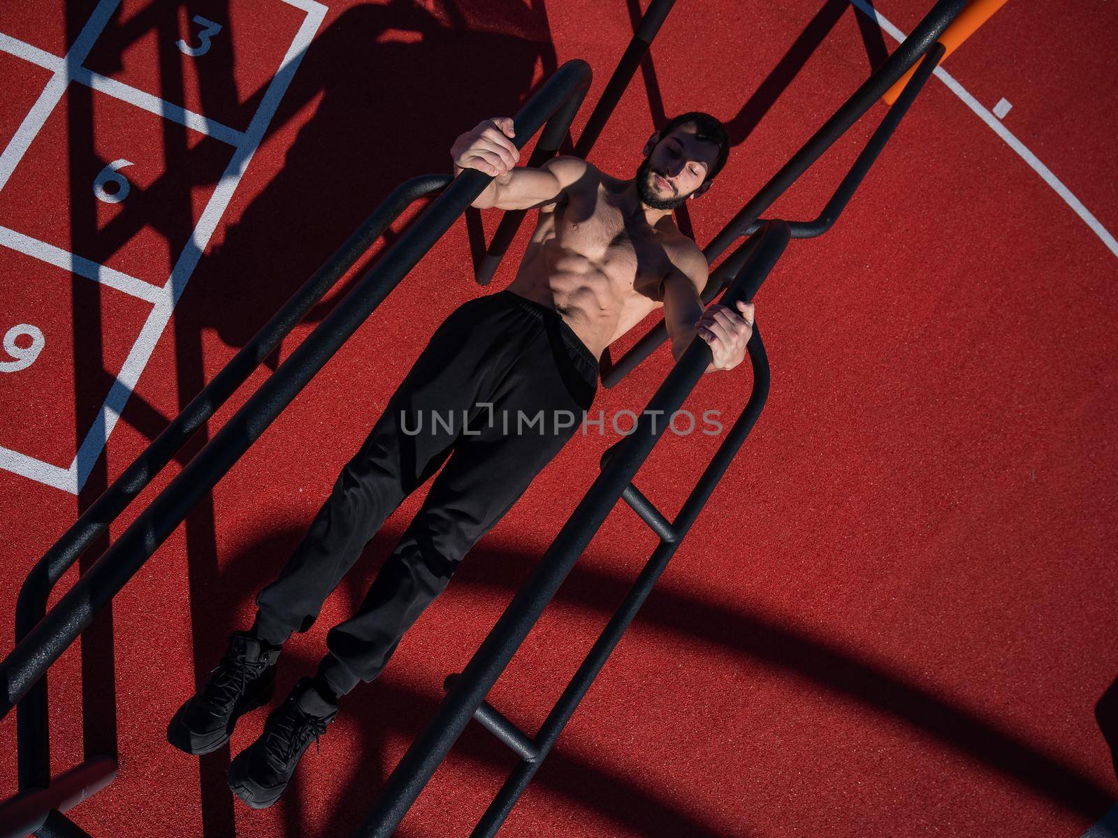 Shirtless man doing balance on uneven bars outdoors. View from above