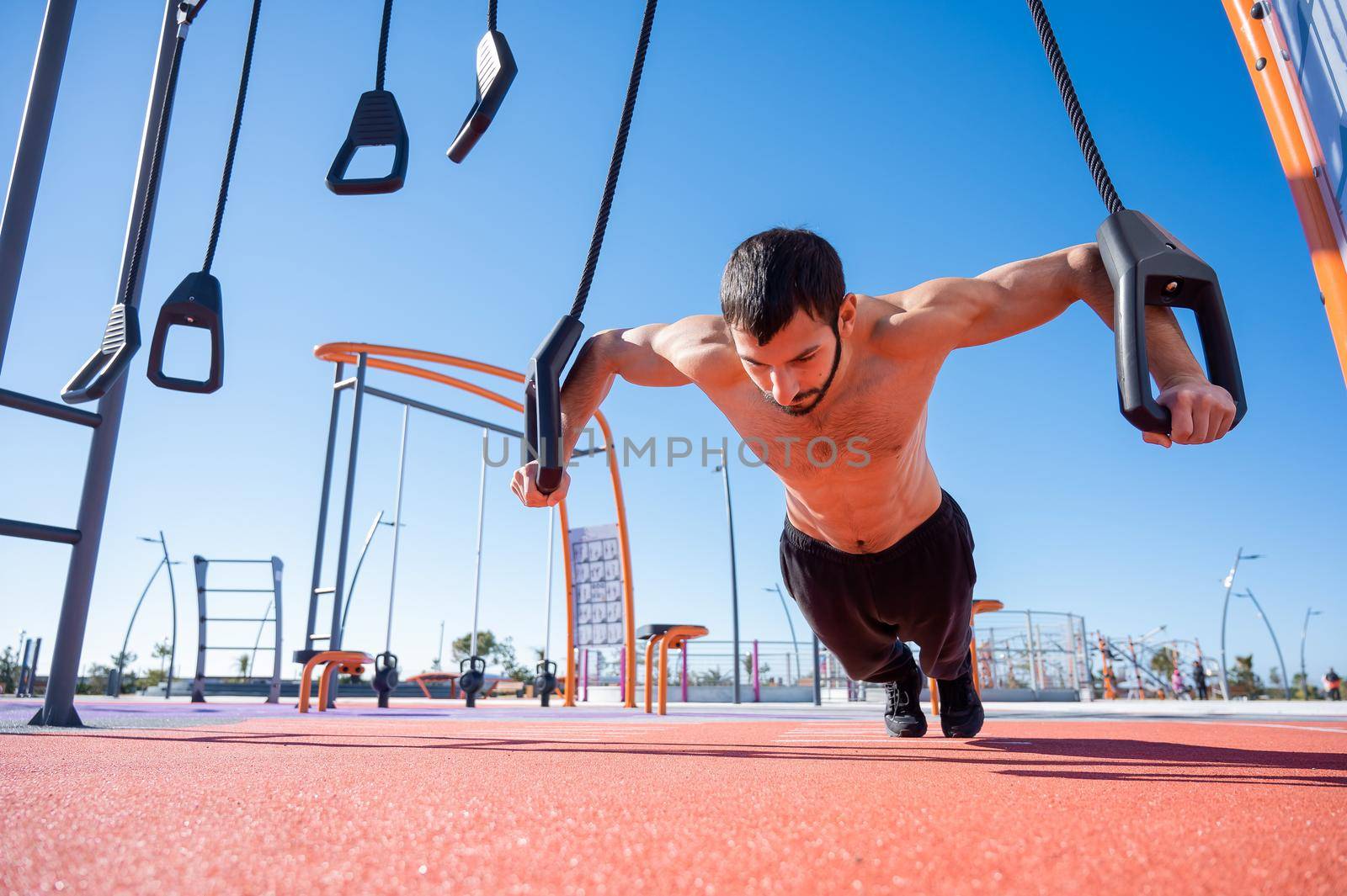 Shirtless man doing loop exercises outdoors