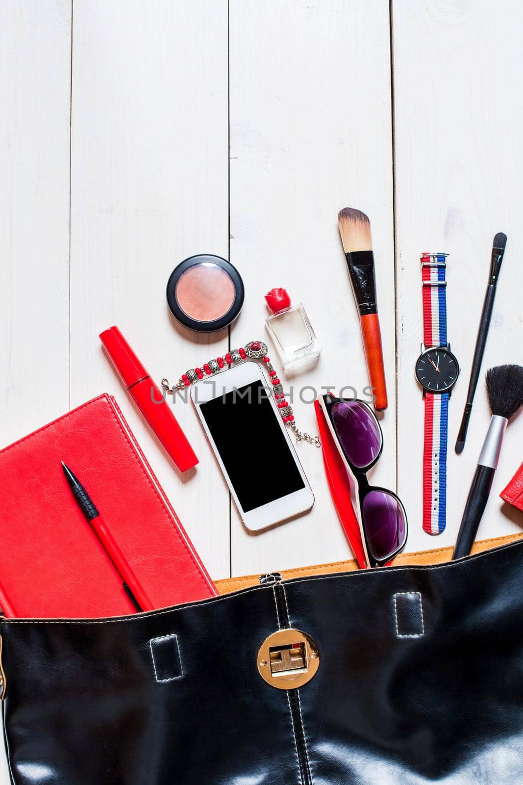 Flat lay, top view, mock up cosmetics and women's accessories fell out of the black handbag on white background. Phone, glasses, watch, notebook, pen