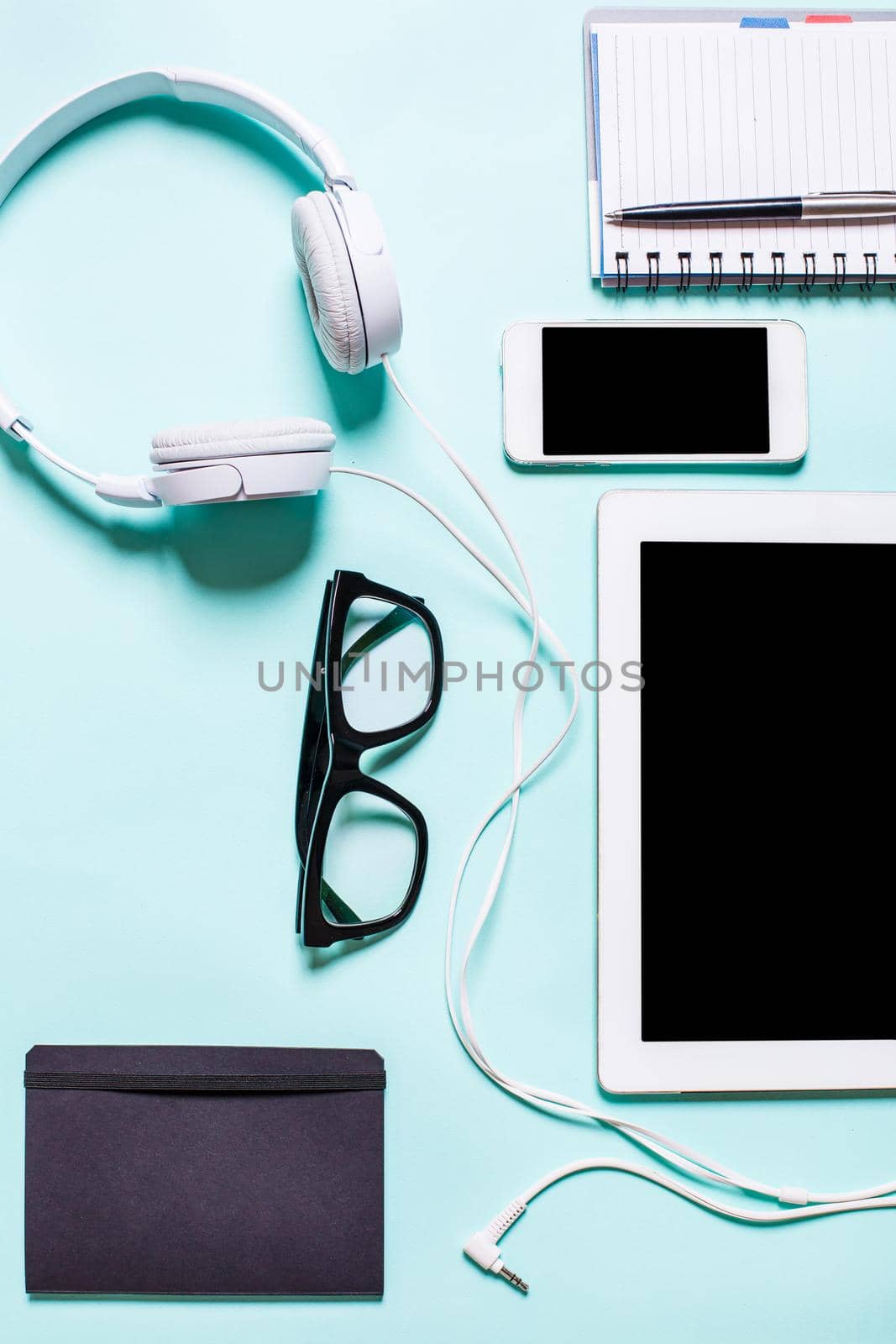 Flat lay, top view, mock up working place with tablet, smartphone, notebook, pen, earphones and glasses on a turquoise background