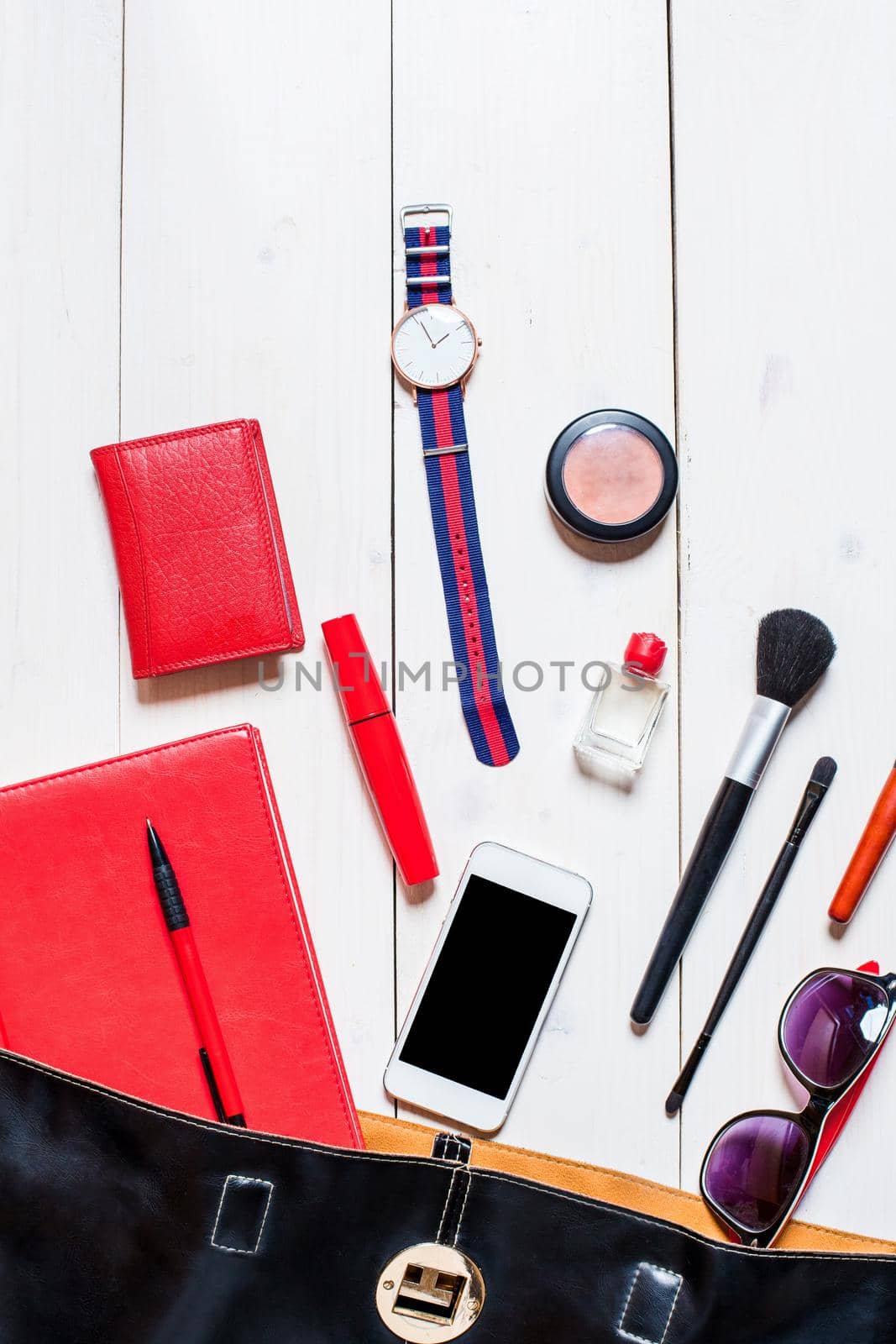 Flat lay, top view, mock up cosmetics and women's accessories fell out of the black handbag on white background. Phone, glasses, watch, notebook, pen