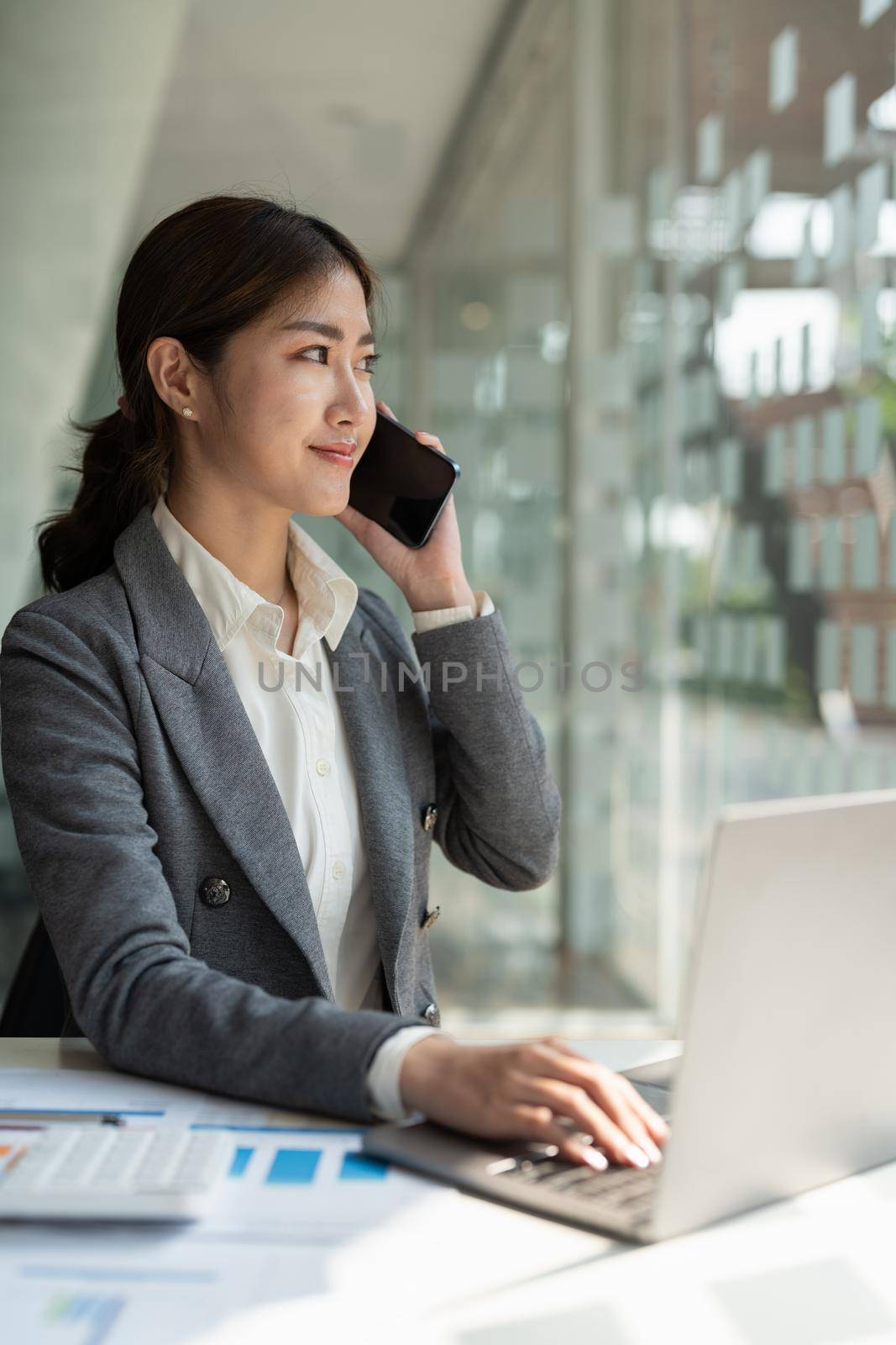 Confident business asian woman in talking consultant on mobile phone at modern office by nateemee