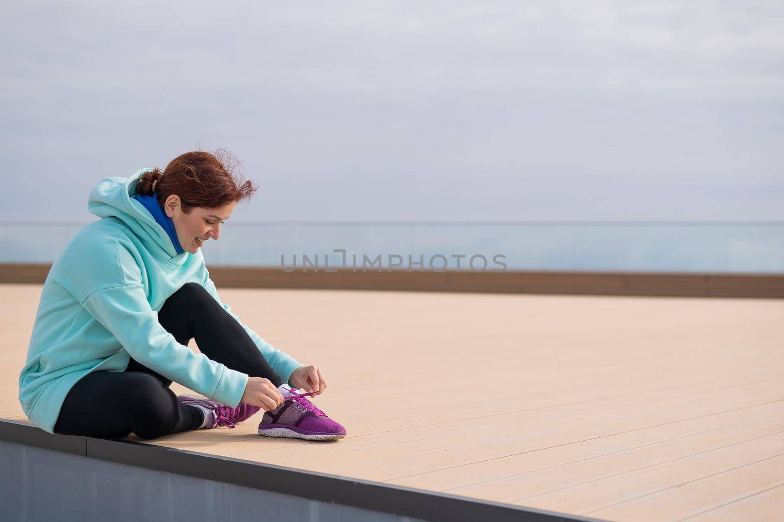 Caucasian woman in a hoodie tying her shoelaces before jogging