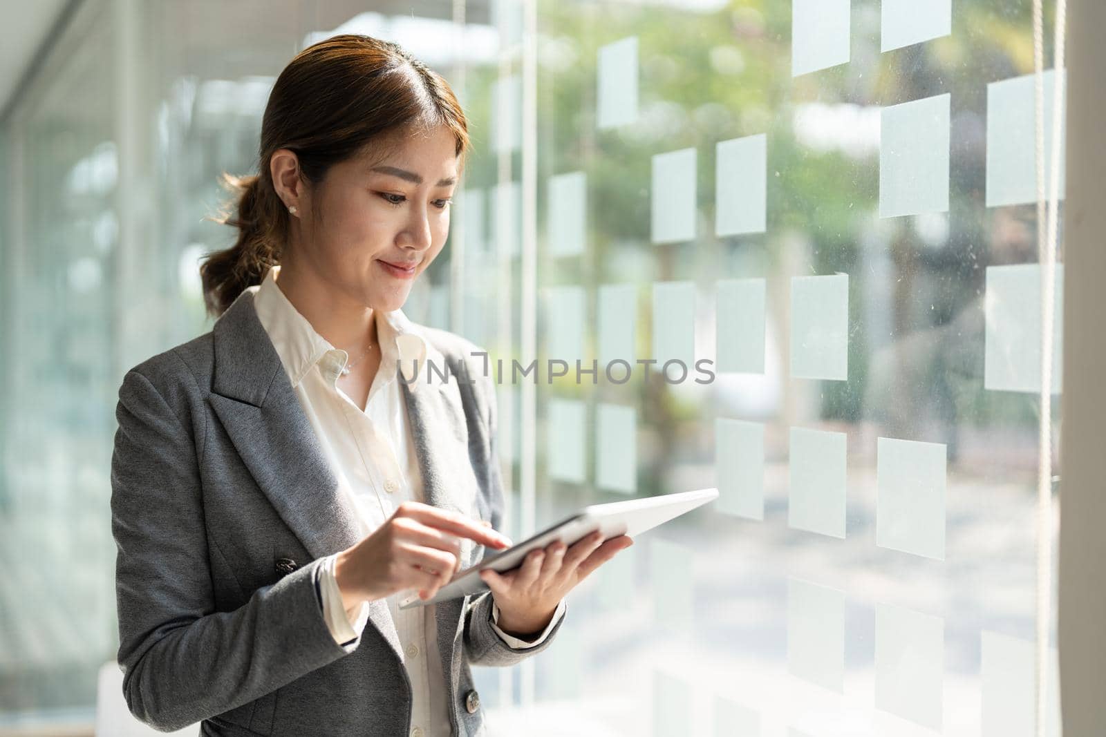 attractive business asian woman standing near window and using smart digital tablet