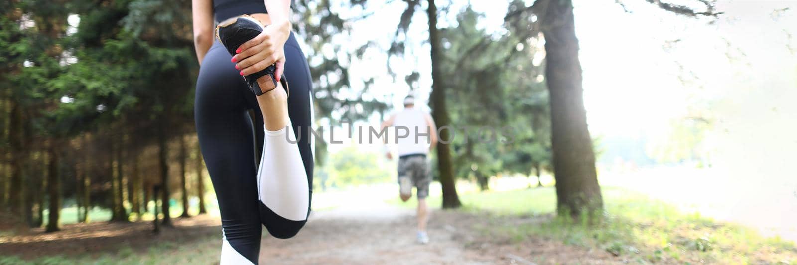 Young athletic woman stretches legs before jogging in park. Warm up before running concept